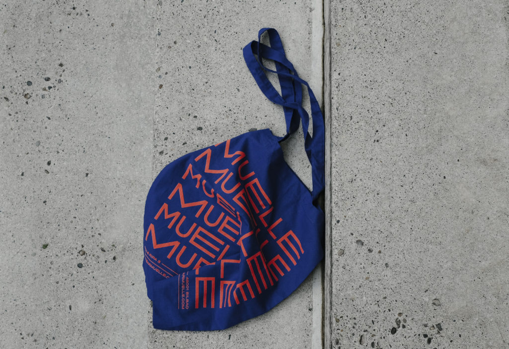 El sistema gráfico de Muelle incluye productos de merchandising como tote bags.